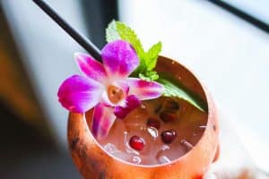 A colorful cocktail garnished with a purple flower and mint leaves.